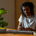 Akai Professional MPK Mini Plus II on a wooden desk with a producer playing
