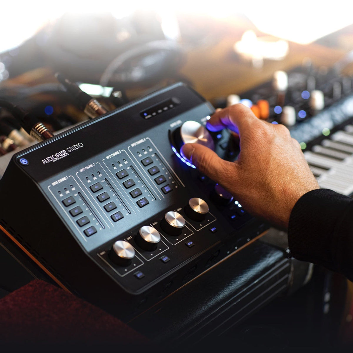 Arturia AudioFuse Studio Rev2 on a studio desk with a hand on the monitor knob