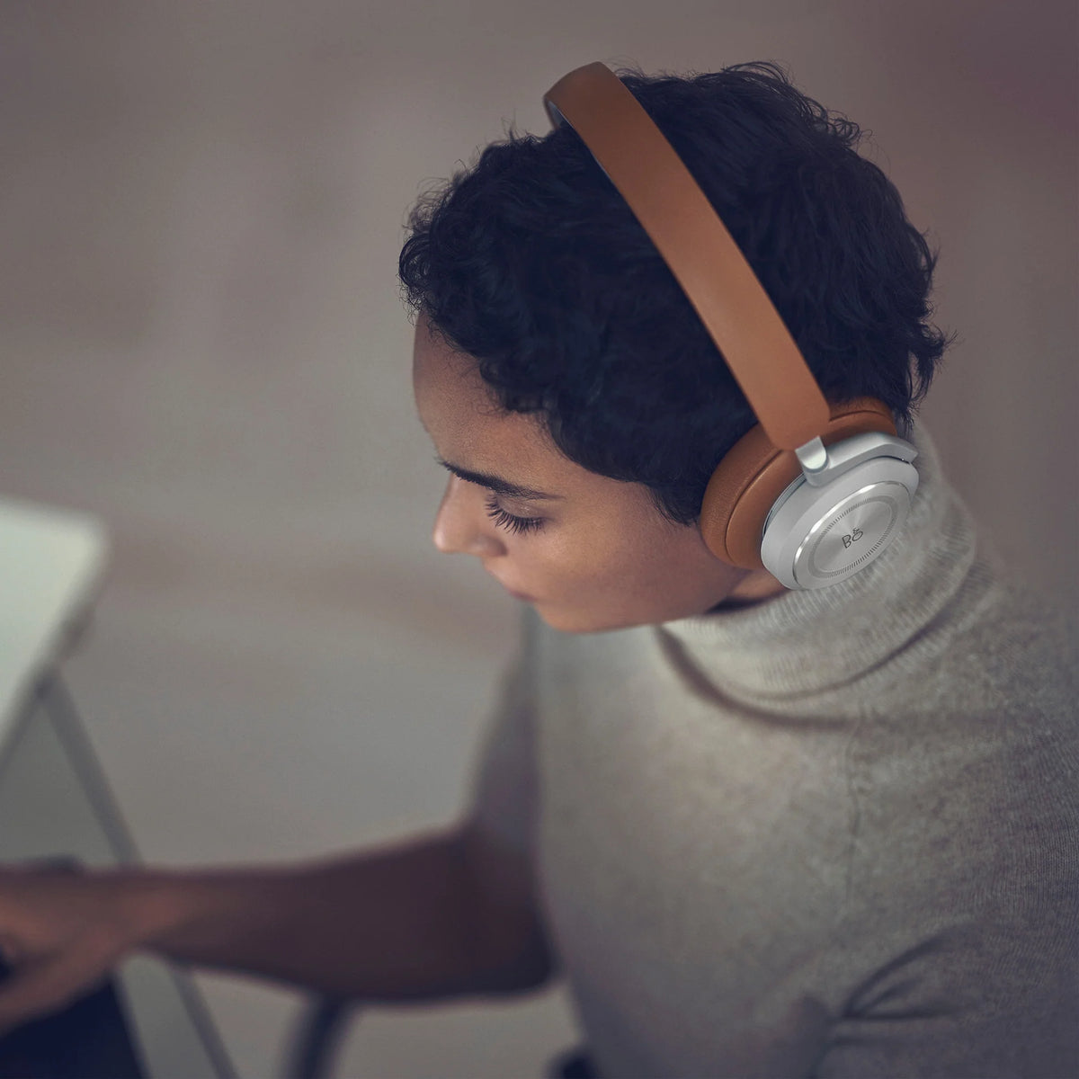 Bang & Olufsen Beoplay HX wireless headphones in timber finish, shown worn in a lifestyle setting with sleek design elements.