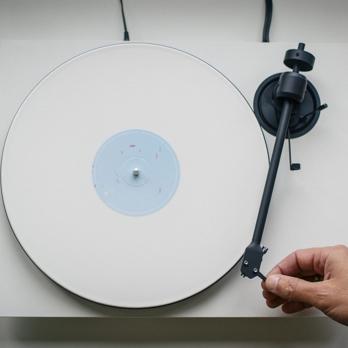 Pro-Ject E1.2 BT Satin White turntable seen from above, a hand guiding the tonearm